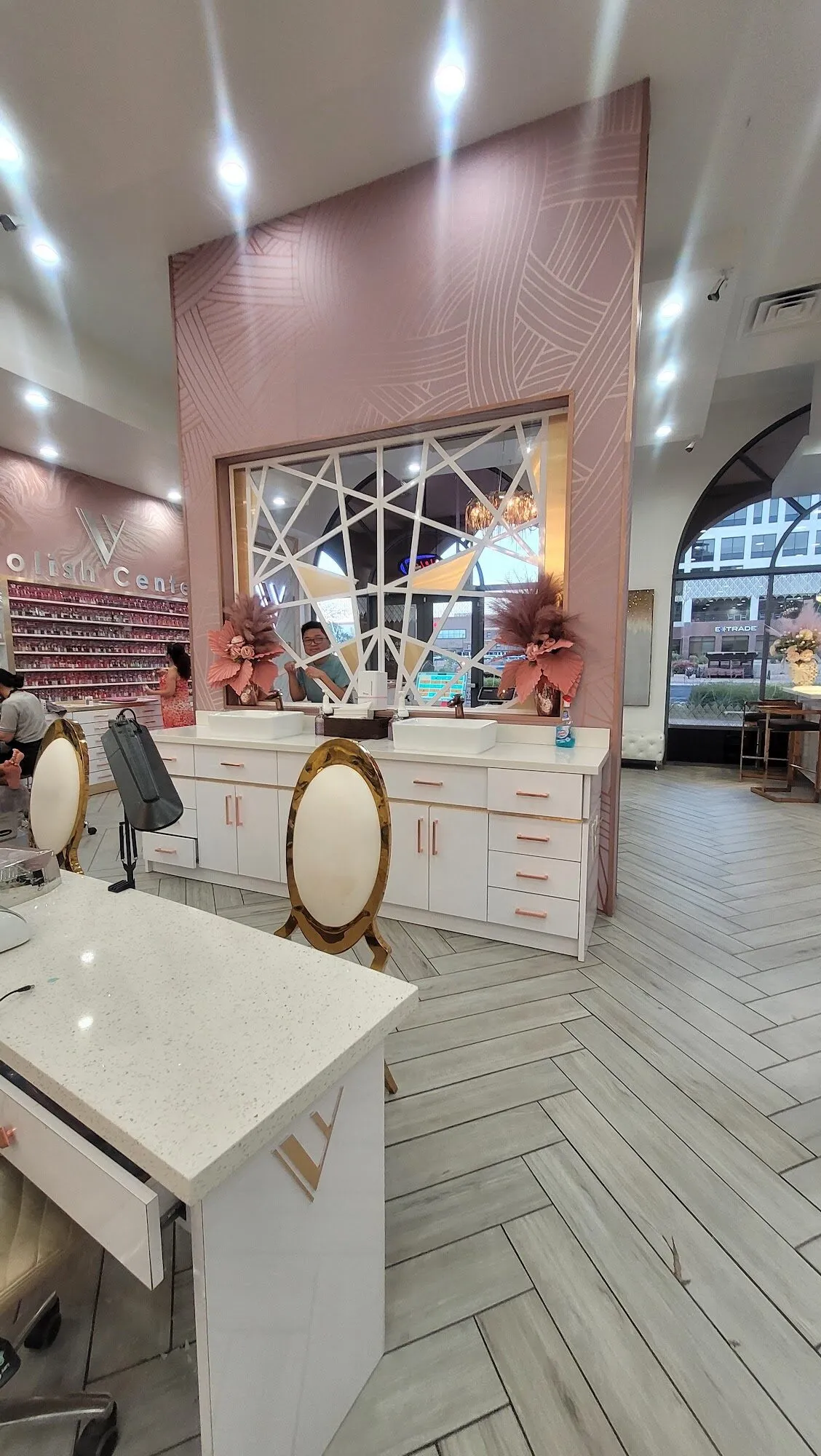 A blush pink feature wall with a geometric mirror above white wash stations at Aria Nail Bar Fashion Square.