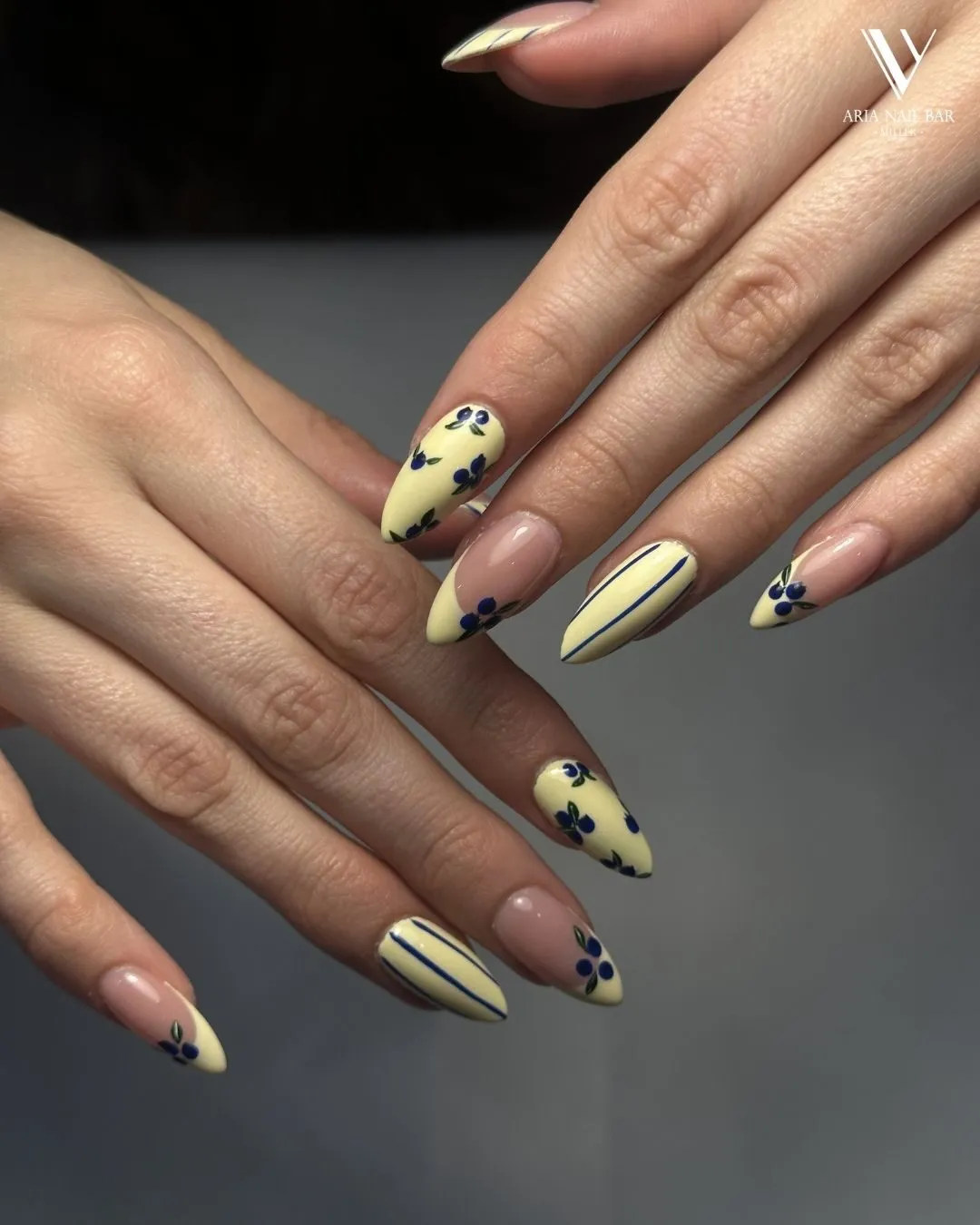 Pale yellow almond nails with hand-painted navy flowers and pinstripes.