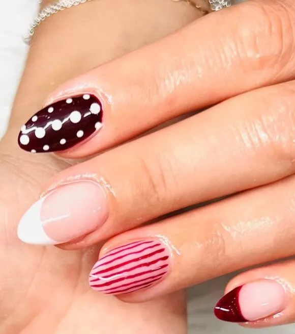 Almond nails mixing burgundy polka dots, red pinstripes, a white French tip and a deep red French tip.