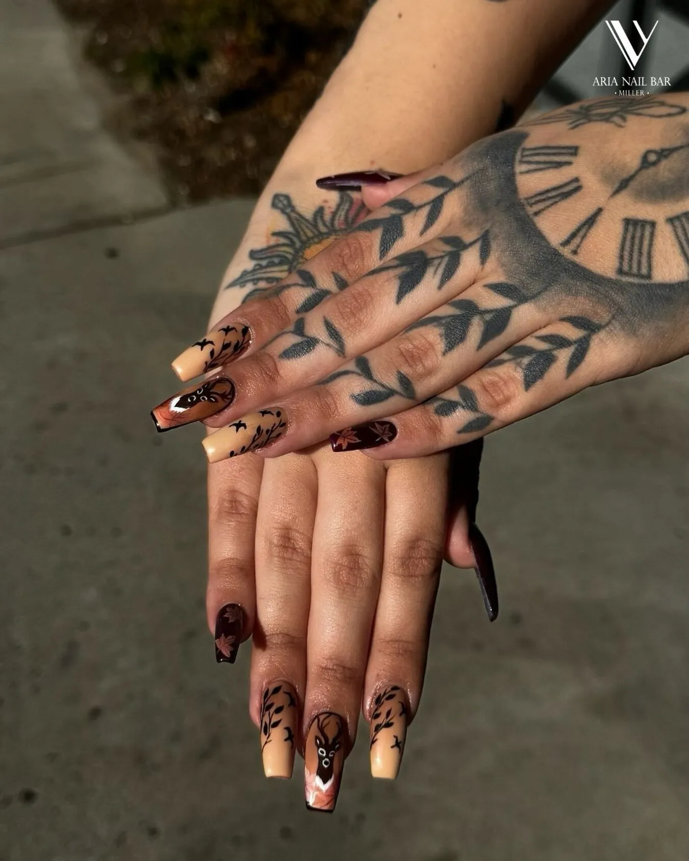 Copper airbrushed square nails with black branch and bat silhouettes, on tattooed hands.