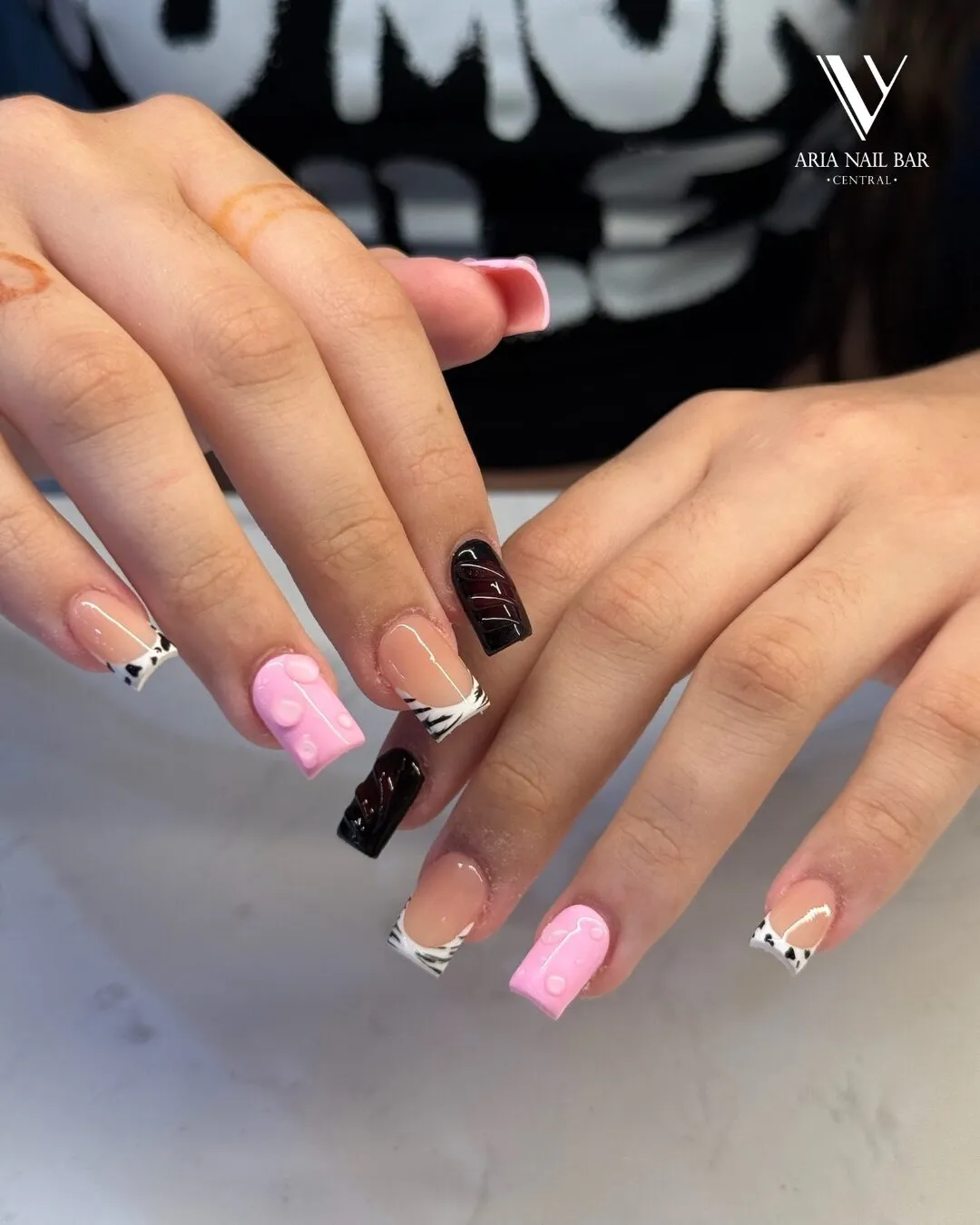 Short square nails mixing bubblegum pink, black-and-white cow print French tips and glossy black accents.