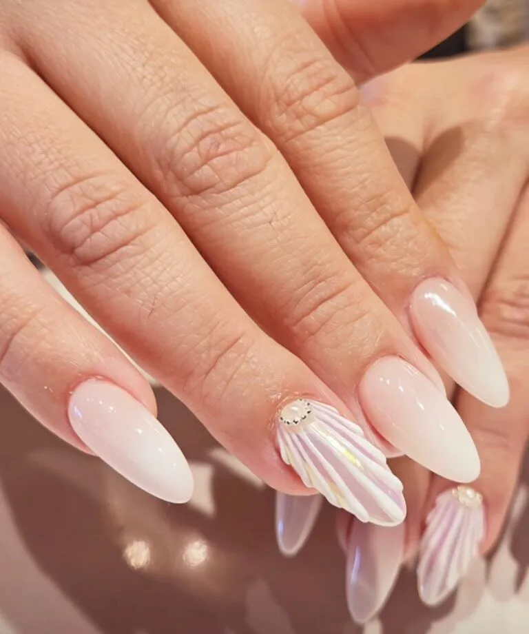 Milky white almond nails with a sculpted 3D seashell accent nail and a single pearl.