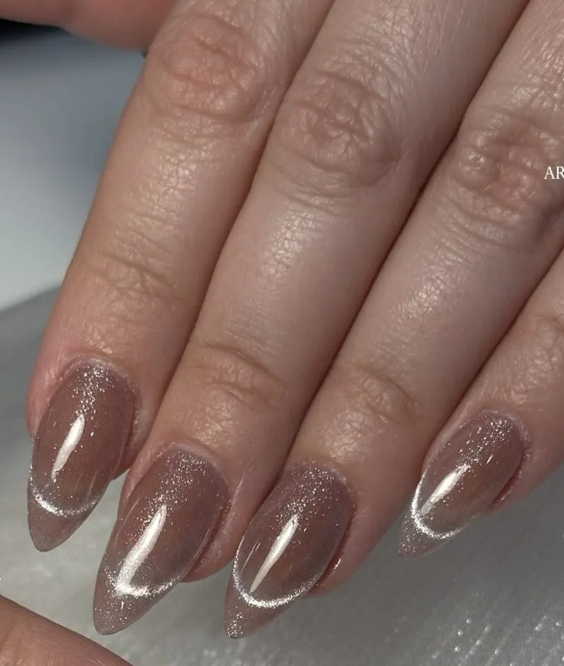 Mocha brown cat-eye nails with a shimmering silver streak on stiletto tips.