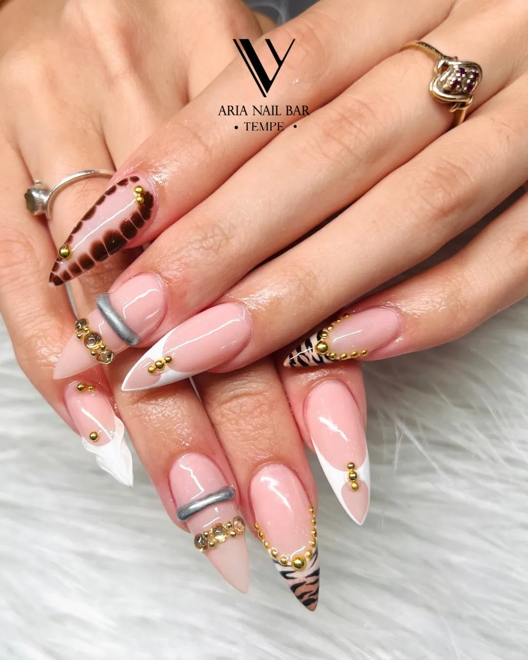 Sheer pink stiletto nails with white deep French tips, tortoiseshell accents and gold studs, styled with gold rings.
