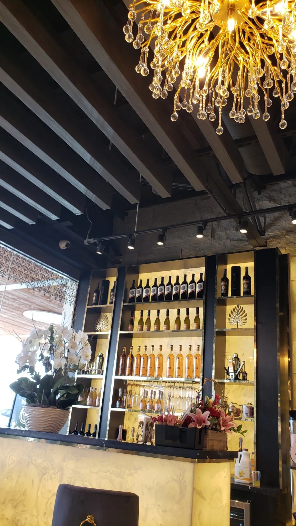 A crystal chandelier above the champagne bar at Aria Nail Bar Phoenix Central, its shelves lined with bottles and glassware.