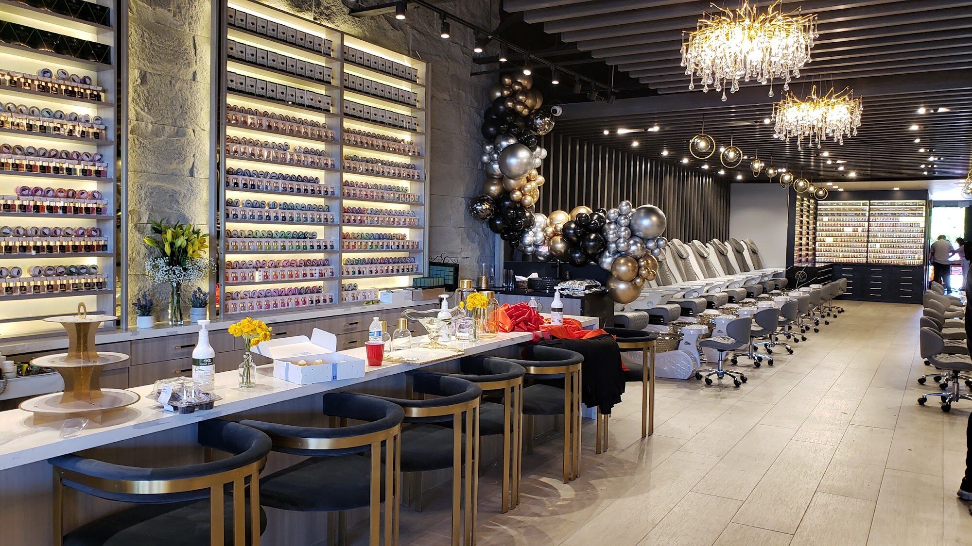 The manicure bar at Aria Nail Bar Phoenix Central, with gold stools, a crystal chandelier and a wall of nail polish.