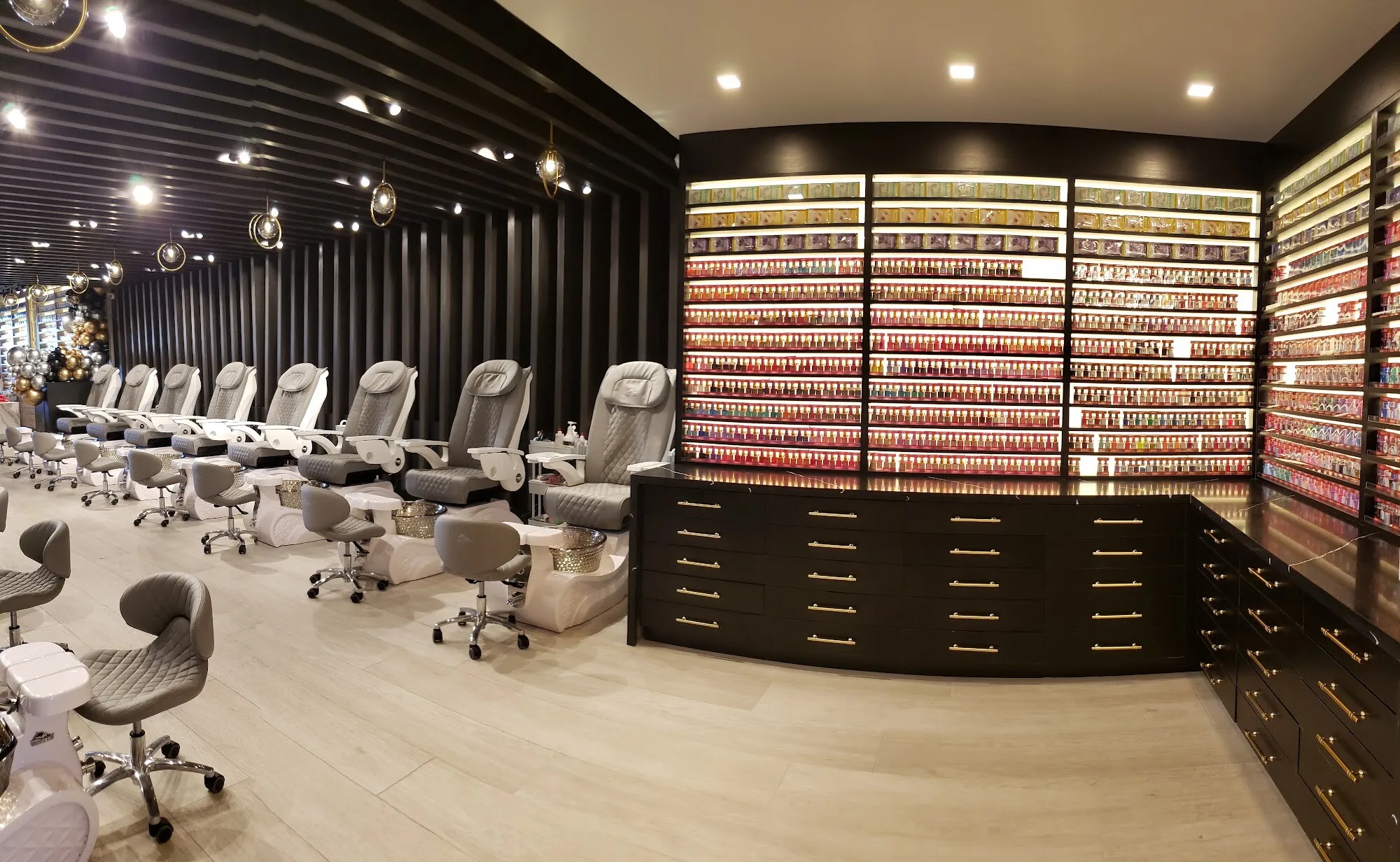 The salon floor at Aria Nail Bar Phoenix Central: white pedicure chairs beneath a black slatted ceiling and a full wall of nail polish.