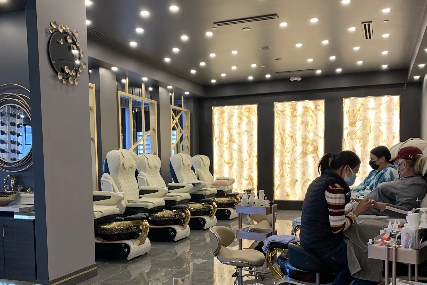 The salon floor at Aria Nail Bar Scottsdale: white pedicure chairs on polished stone beneath glowing backlit onyx panels.