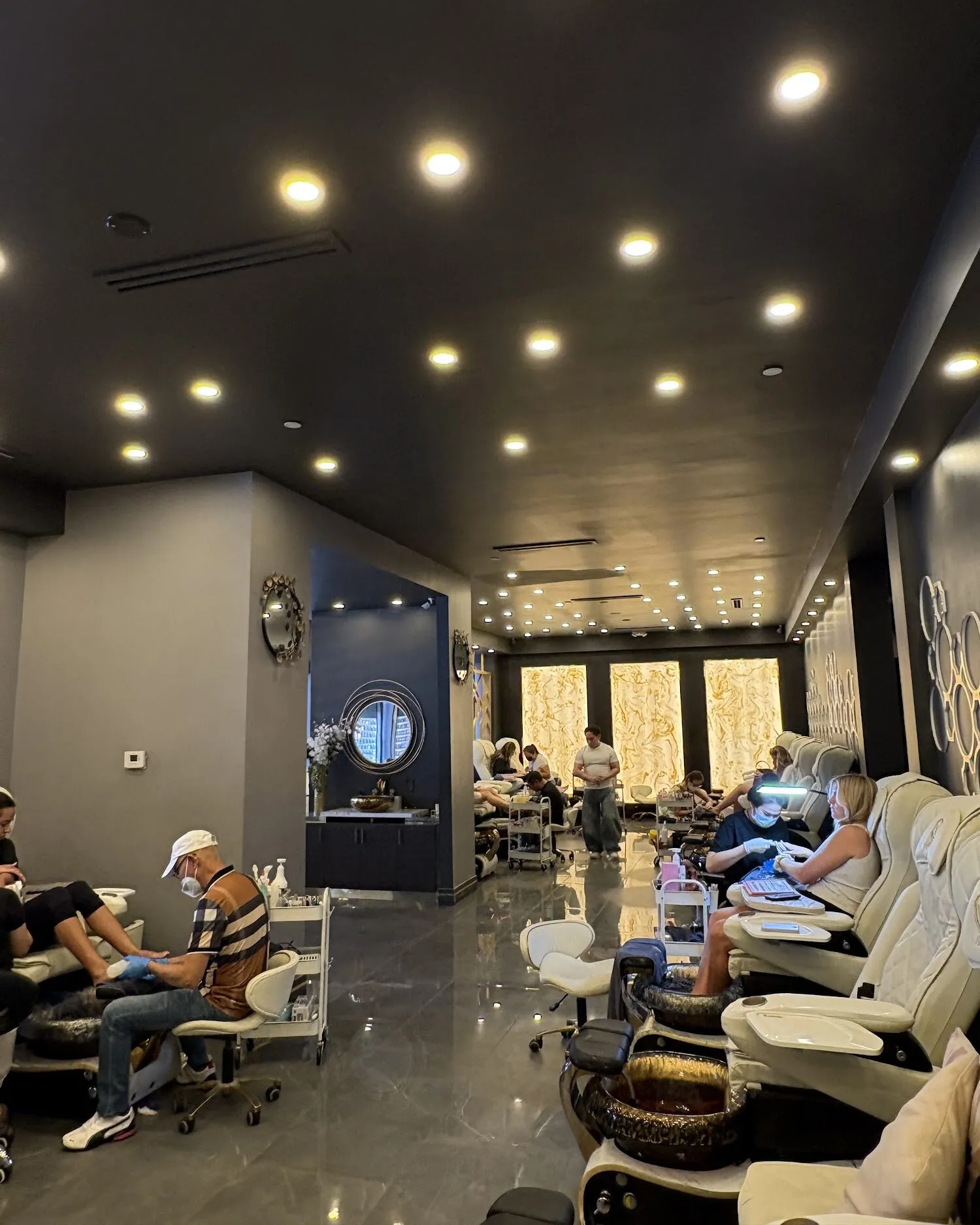 Looking down the salon at Aria Nail Bar Scottsdale toward the glowing onyx panels, with guests settled into the pedicure chairs.