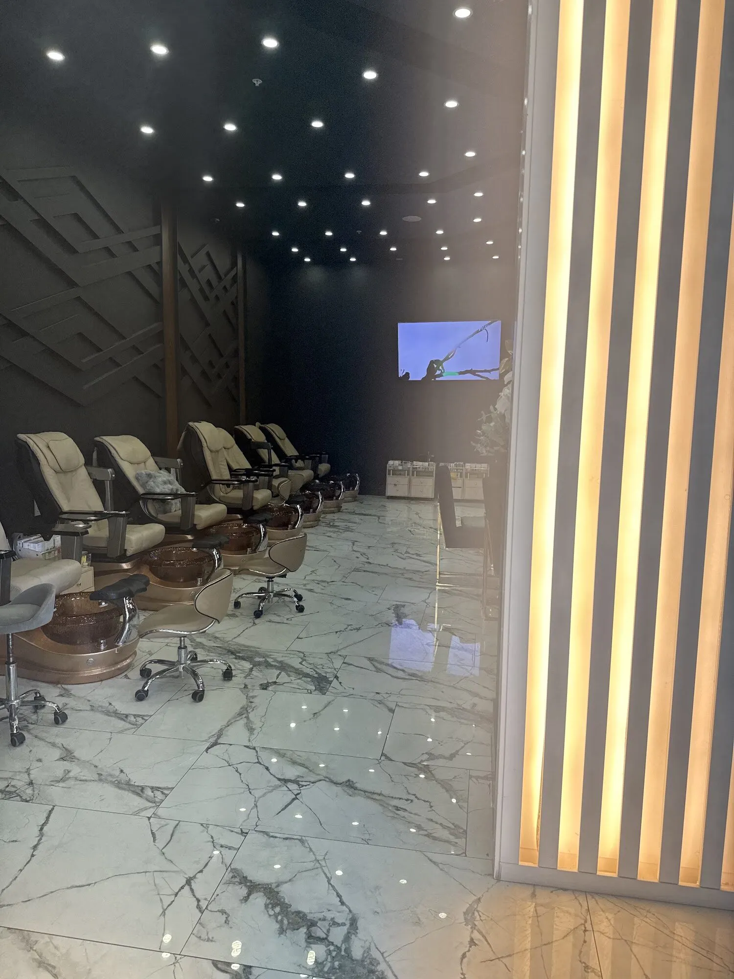 A backlit slatted wall beside cream pedicure chairs on marble floors at Aria Nail Bar Tempe.