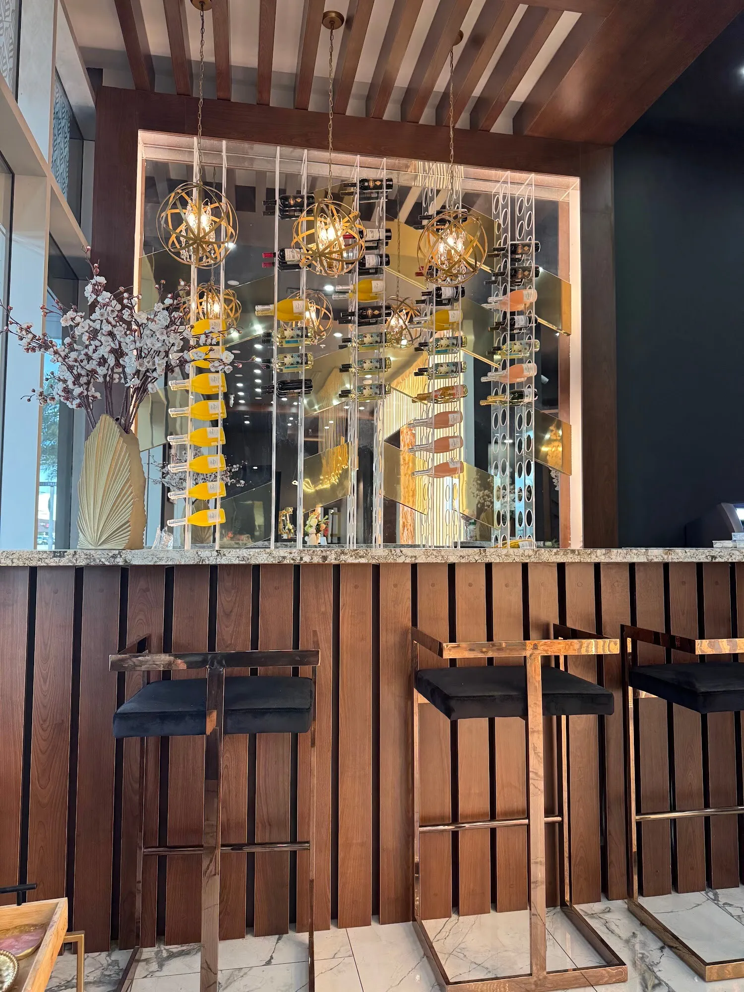 The walnut bar at Aria Nail Bar Tempe with gold stools beneath a cluster of gold chandeliers.