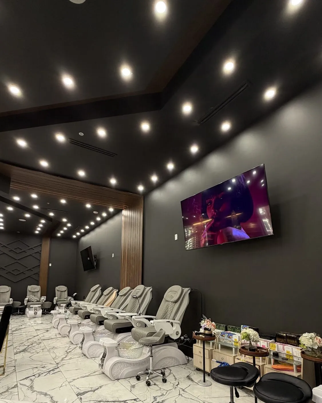 Pedicure chairs beneath a dark ceiling of spotlights at Aria Nail Bar Tempe, with marble floors and a wall-mounted screen.